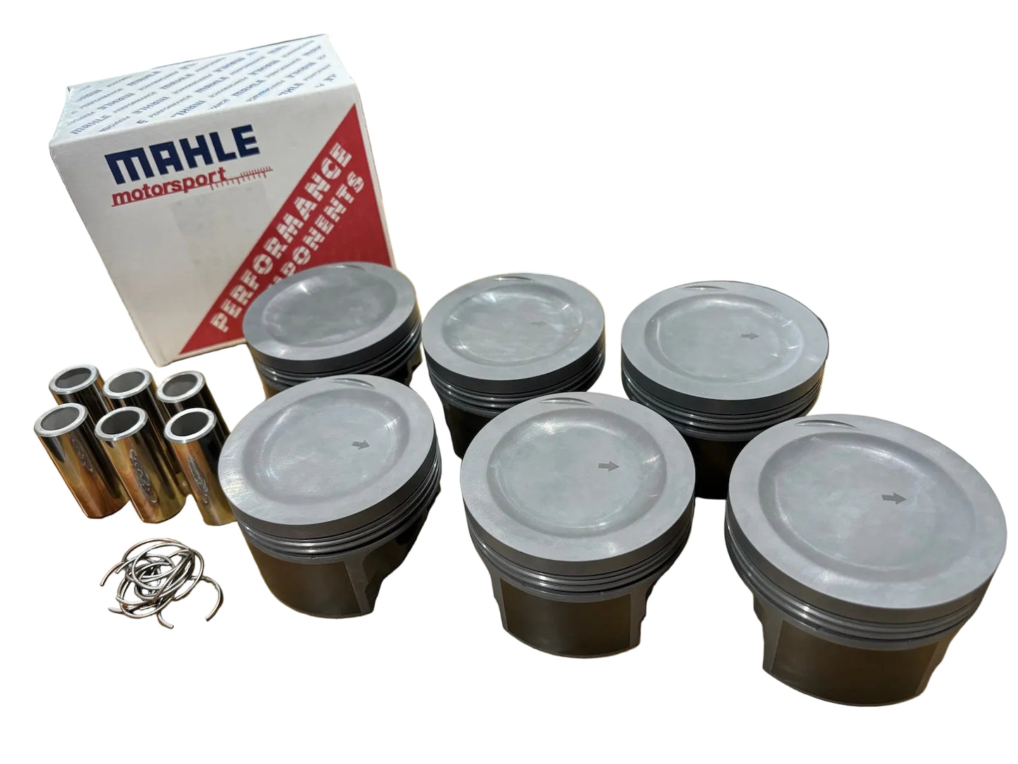 A set of new pistons displayed in front of their packaging box, which has the text 'Mahle Motorsport PERFORMANCE PARTS' on it. For BMW M20B27 325e engine.