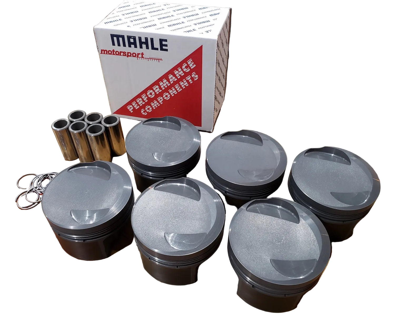 A set of Mahle Motorsport BMW M20 pistons displayed on a table with the Mahle box visible in the background.