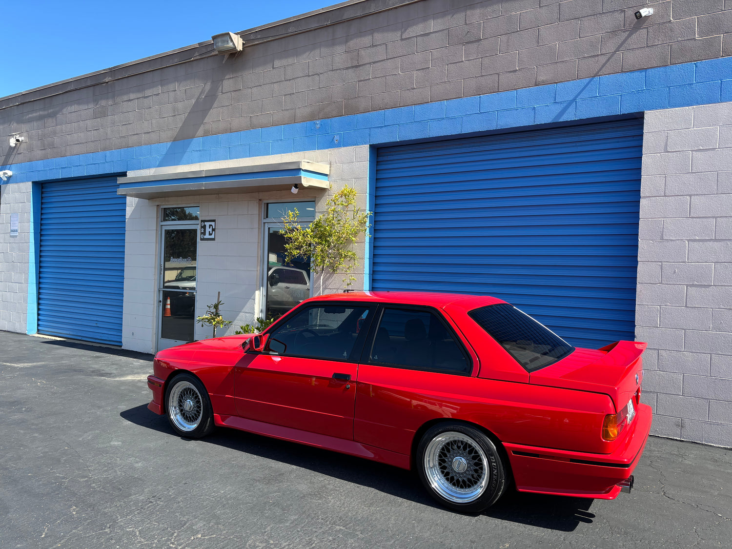 Red BMW E30 M3 parked in front of the BimmerHeads shop in Grover Beach, California.
