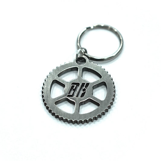 A stainless steel key tag with a gear design and the letters 'BH' in the center, attached to a keyring.